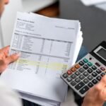 Pessoa analisando extratos bancários com uma calculadora, ilustrando o conceito de como economizar dinheiro através do diagnóstico financeiro