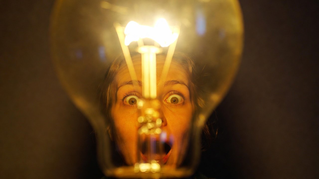 Pessoa com uma expressão de eureka, com uma lâmpada acesa ao fundo, simbolizando o momento de ter uma ideia de negócio